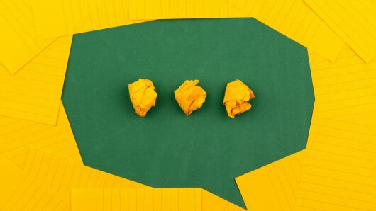 Drei zerknüllte gelbe Zettel in einer grünen Sprechblase, umgeben von gelben Haftnotizen.